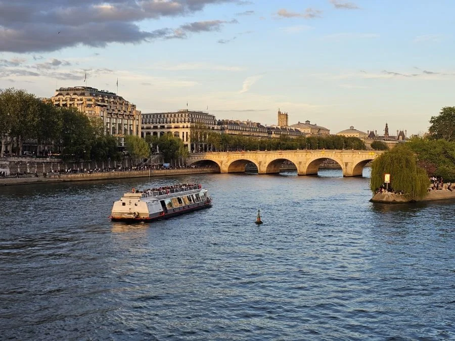 A boat floats down the Seine river in Paris with a bridge behind it