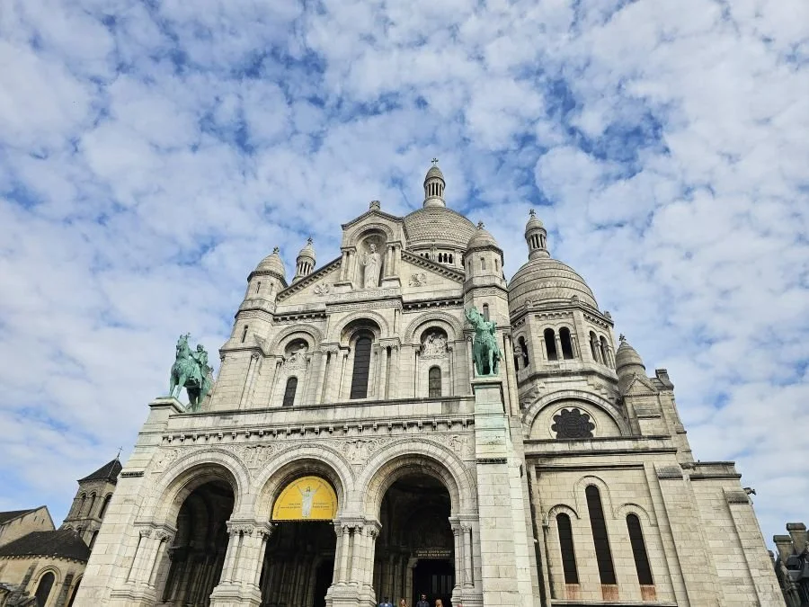 The front of a white church in Paris under a cloudy blue sky