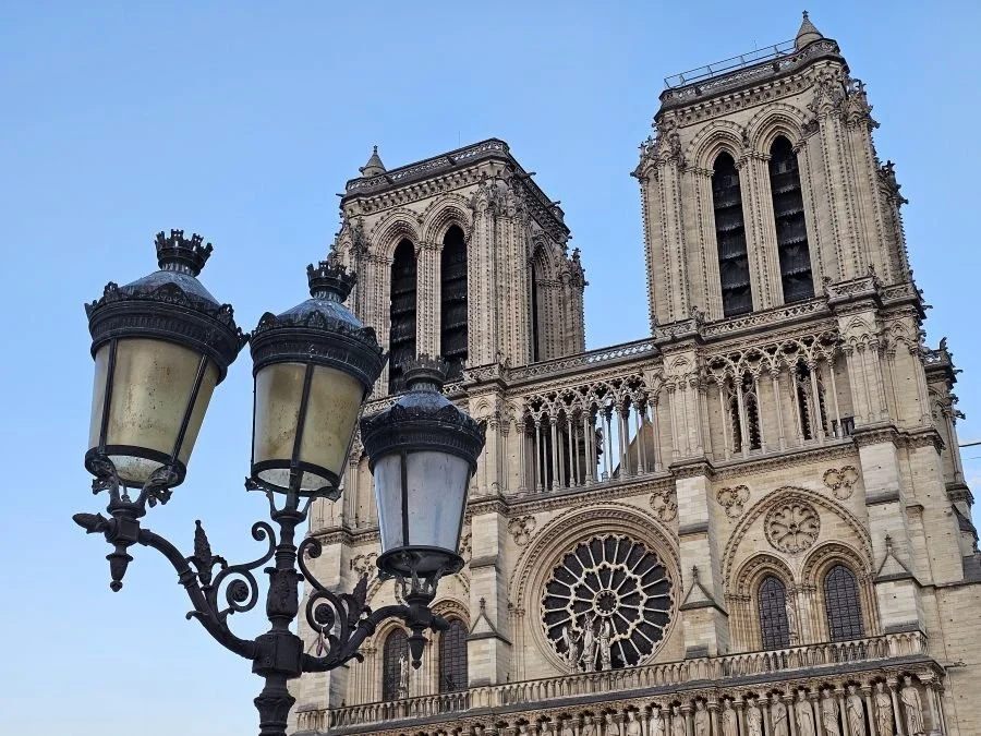 The two towers of the Notre Dame Cathedral up close with a street lantern in the foreground.