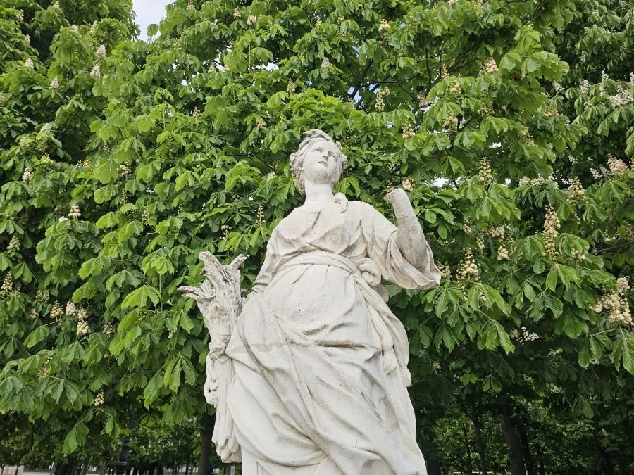 White statue of a woman against greenery in a garden in Paris