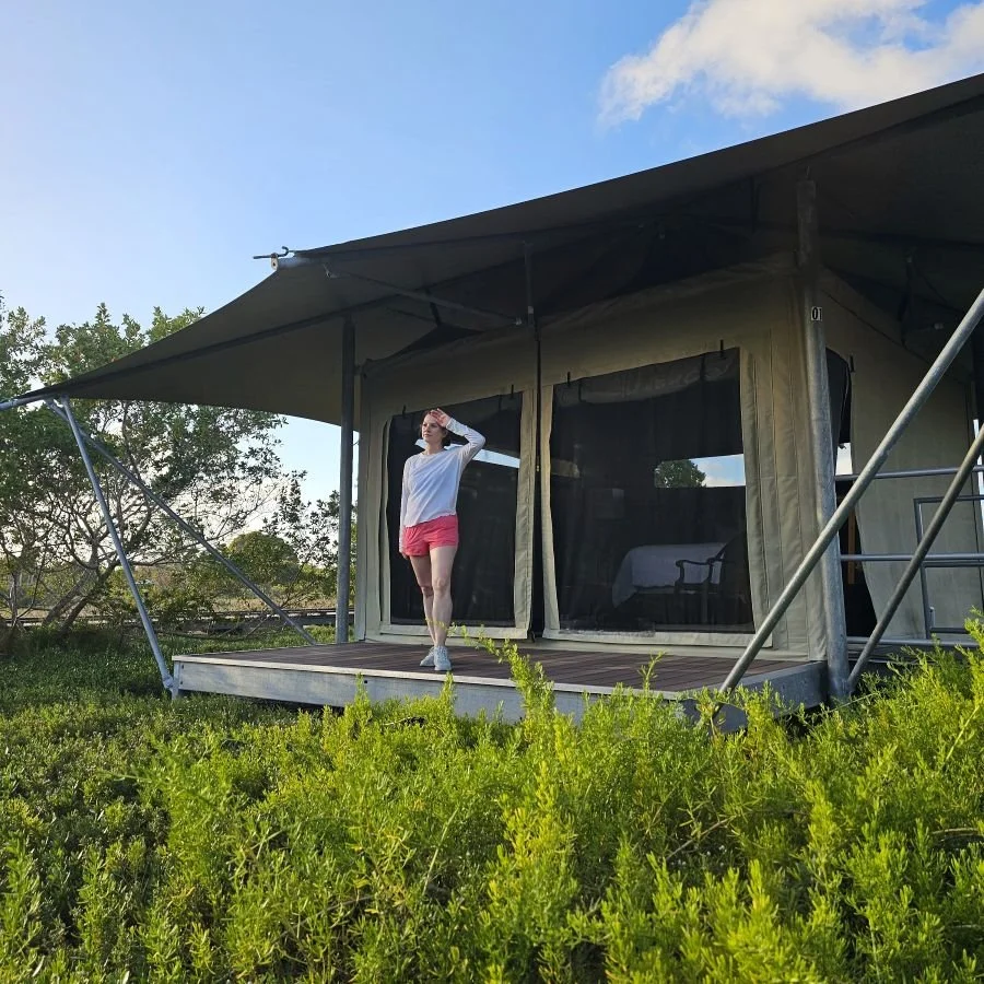 A woman in a white shirt and red shorts stands on a deck outside a canvas glamping tent in the Everglades