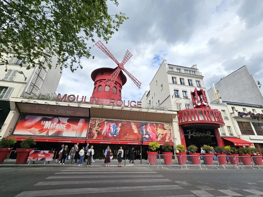 A city block of white buildings with the Moulin Rouge red windmill in the center in the Montmartre neighborhood of Paris.