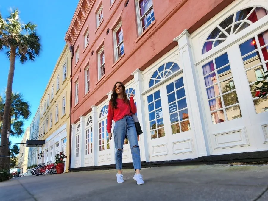 A woman in jeans and sweater walking down a colorful street on a Charleston girls trip
