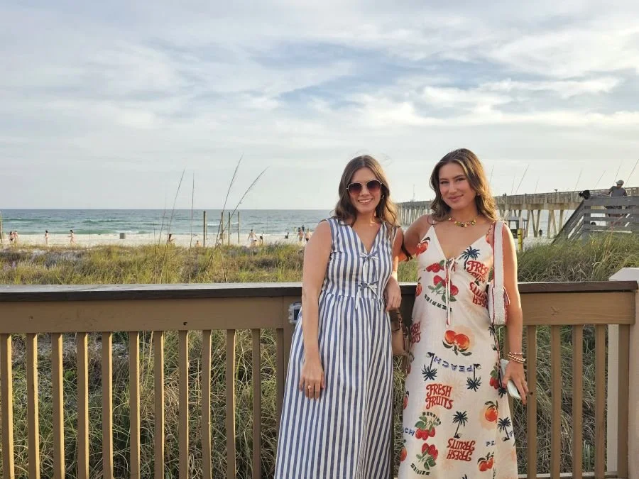 A Panama City Beach girls trip in Florida with two women standing on a boardwalk with the ocean behind them.