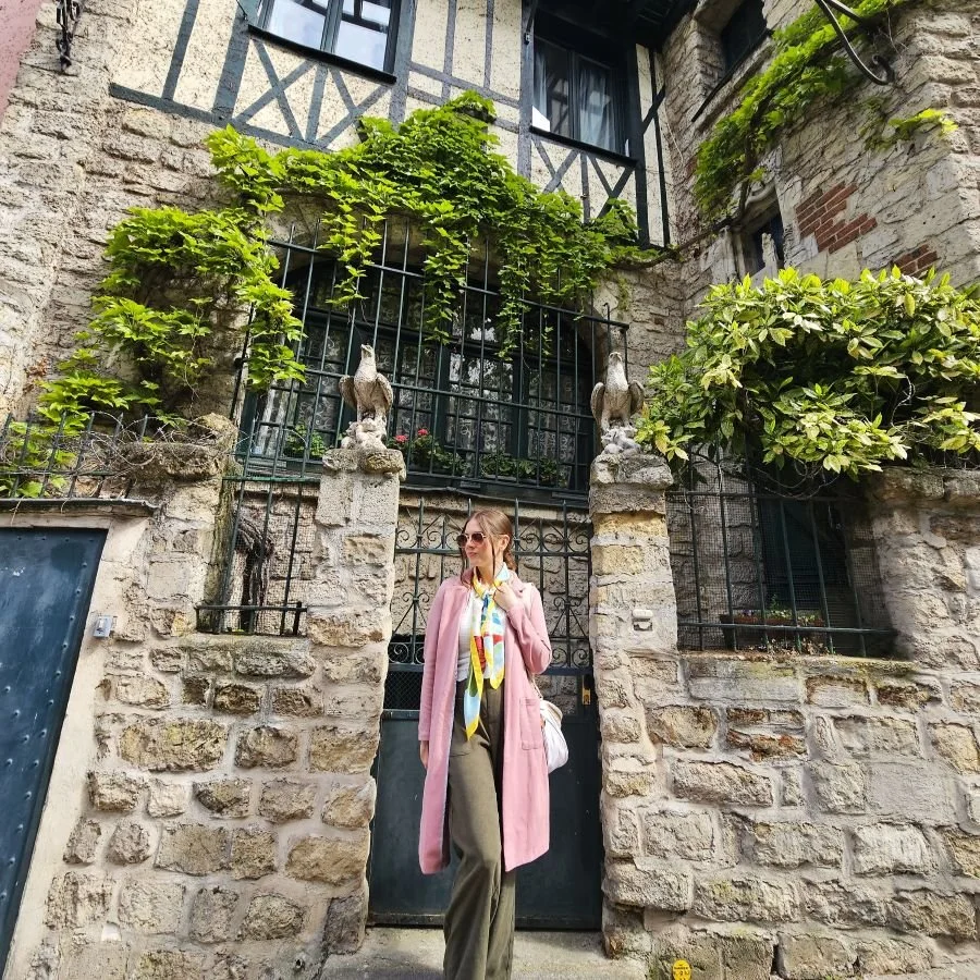 A woman in a pink coat stands in front of a stone wall in Montmartre in Paris