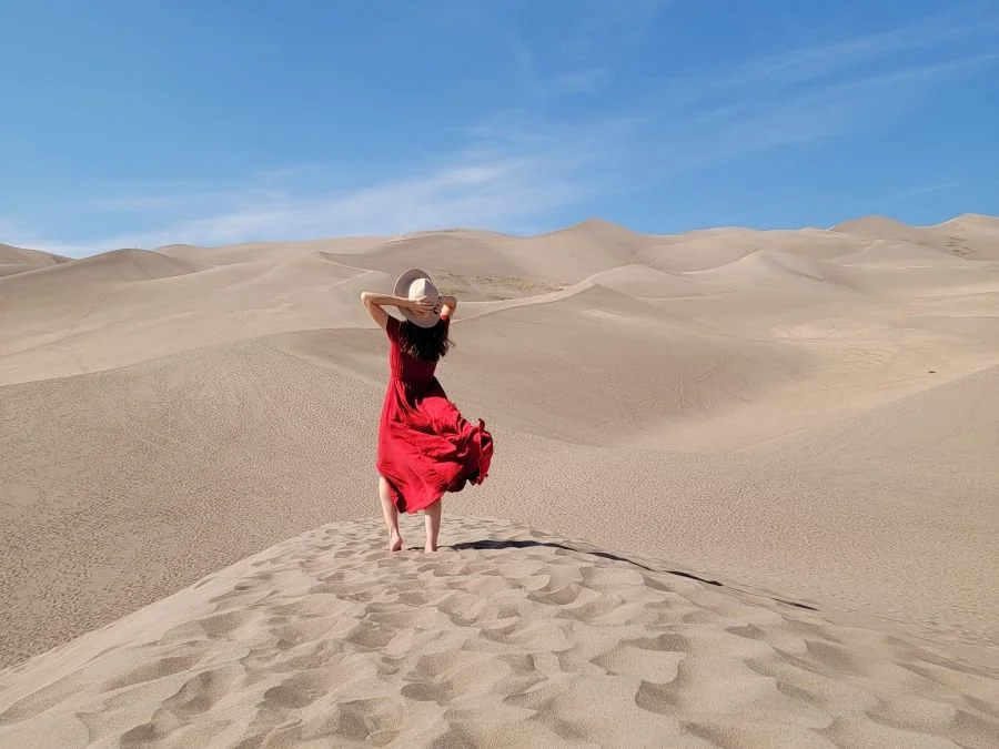 A woman in a red dress stands on a sand dune in Colorado
