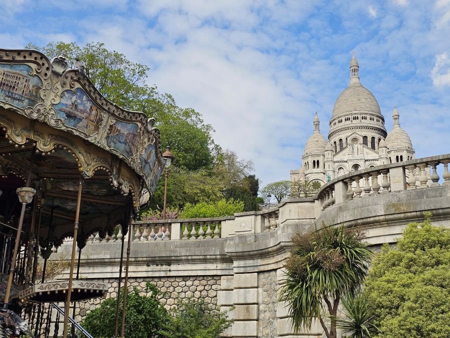 A carousel sits below a white church building in Montmartre Paris