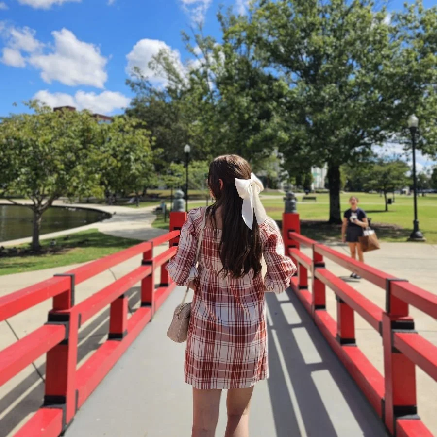 A woman in a dress and hairbow walks across a red bridge to a park in Huntsville