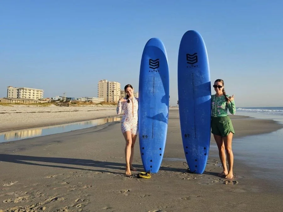 Two women standing by blue surfboards on the beach on a Florida girls weekend in Jacksonville.