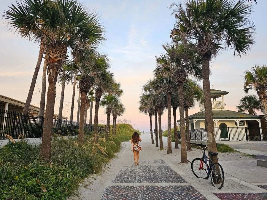 A woman walks under palm trees toward the beach on a girls trip in Florida
