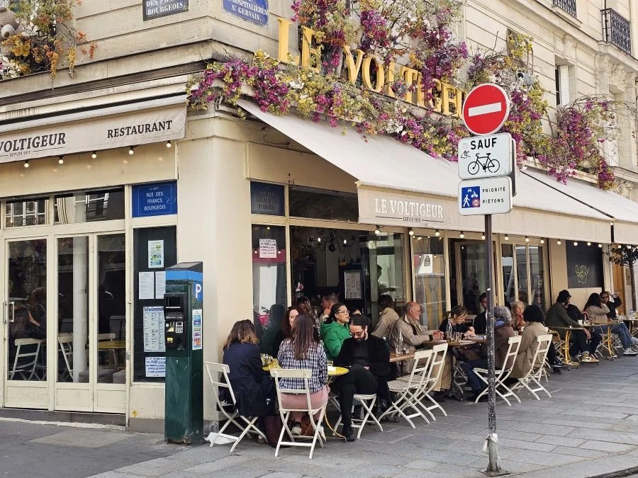 A sidewalk cafe with floral decorations above the awning in Paris