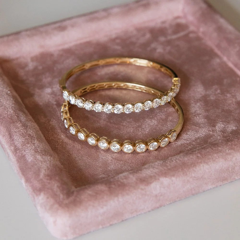 Three gold bracelets with diamonds resting in a pink velvet jewelry display.