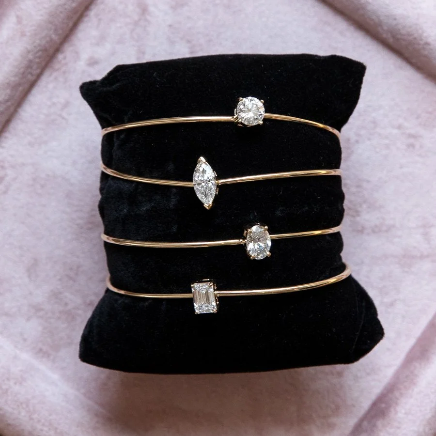 Lab diamond gold rings sit on a black pillow on a pink velvet background