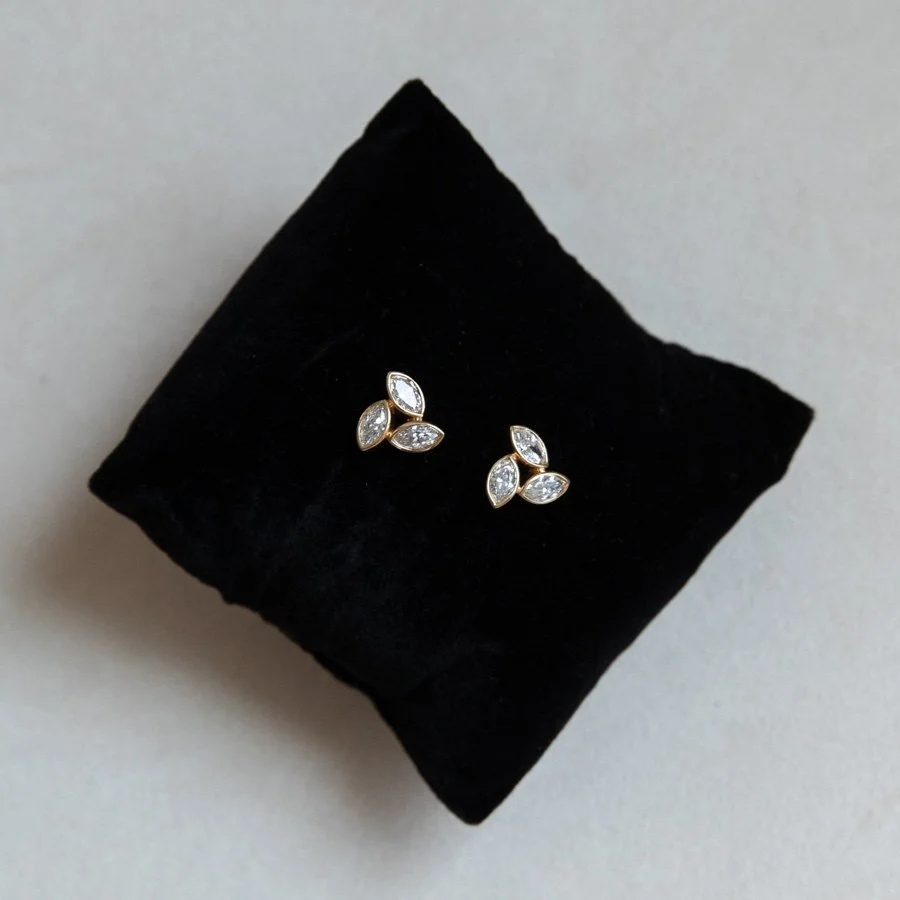 Diamond cluster earrings sit on a black pillow on a grey background.