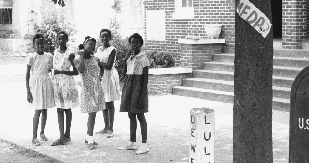 Five African-American girls from Hattiesburg, Mississippi pose for the camera in front of True Light Baptist Church during Freedom Summer, 1964. They are (from left to right) Otis Ruth Travis, Veronica Carter, Glenda Polk, Dorothy Jean Patton, and Joyce McGowan. Affixed to the tree near the girls is a handmade sign for the Mississippi Freedom Democratic Party (MFDP). © 1964 Herbert Randal Freedom Summer Photographs, McCain Library and Archives, The University of Southern Mississippi.