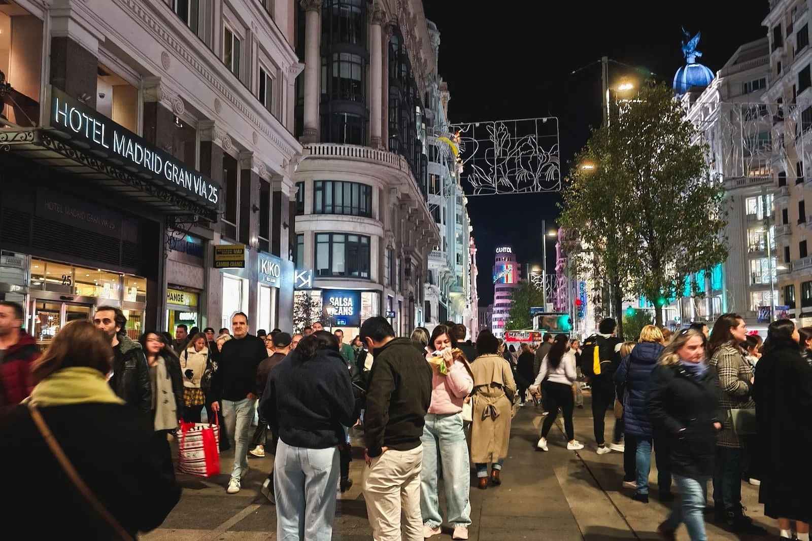 Gran Vía in Madrid illuminated at night with traffic and people walking through the city.