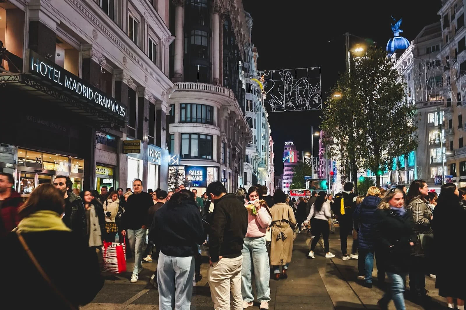Nighttime street scene on Gran Vía in Madrid with crowds, lights, and shops.