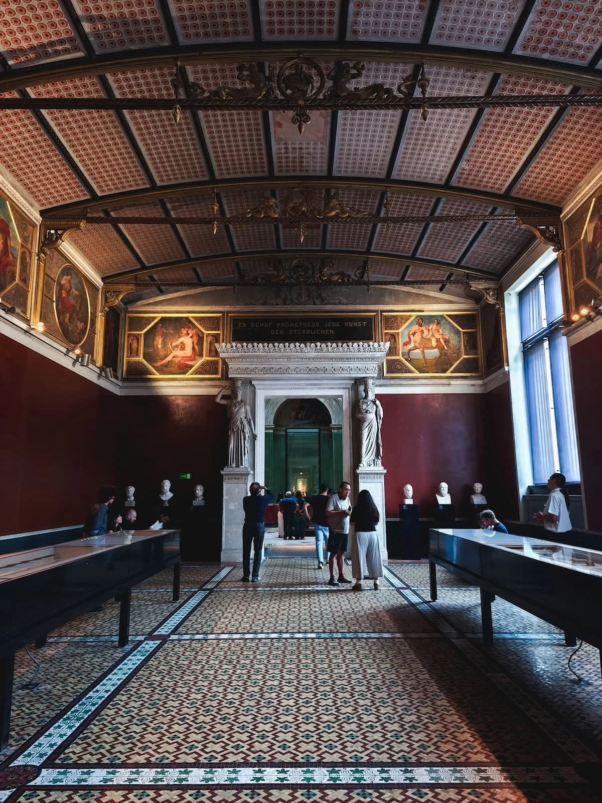 Historic museum gallery with ornate ceiling decoration and exhibition displays inside Berlin's Neues Museum.