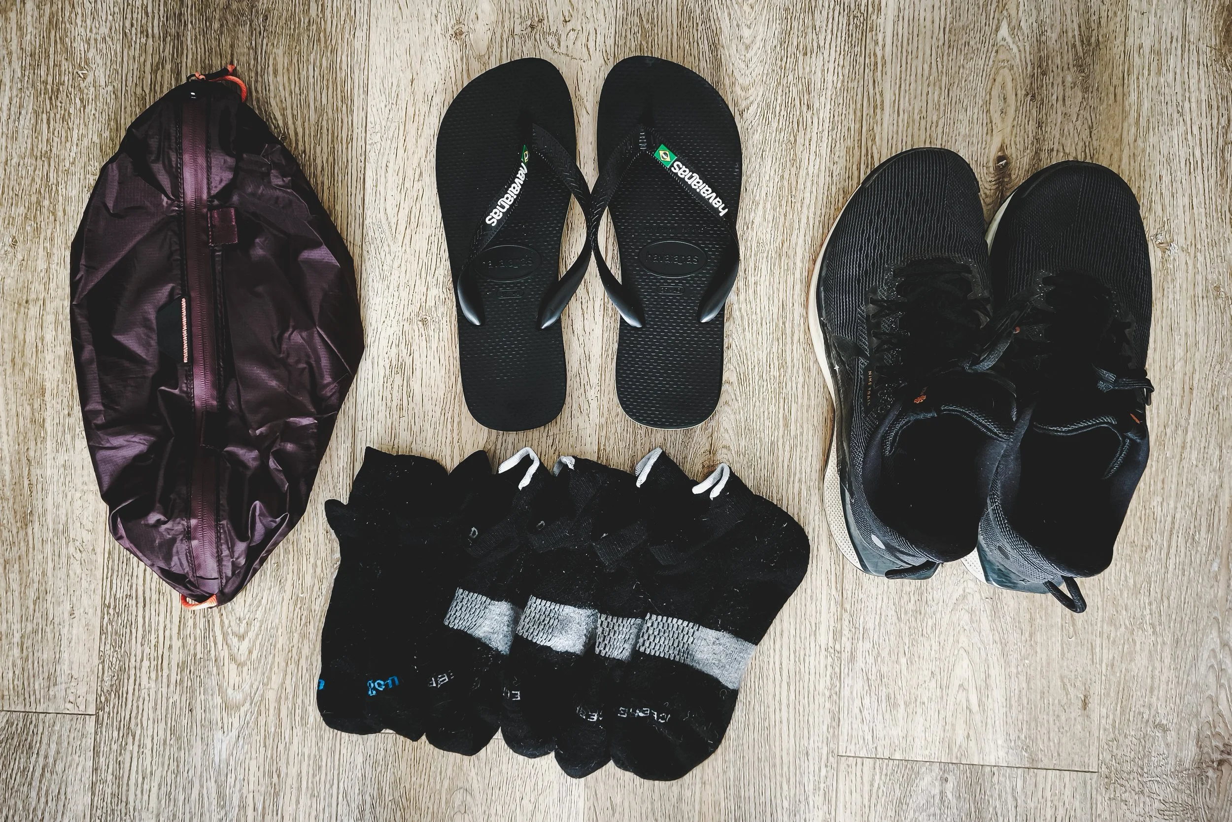 Flat lay of my shoe set-up, with a pair of trail runners, a pair of flip-flops, 3 pairs of merino wool socks, and a shoe bag.