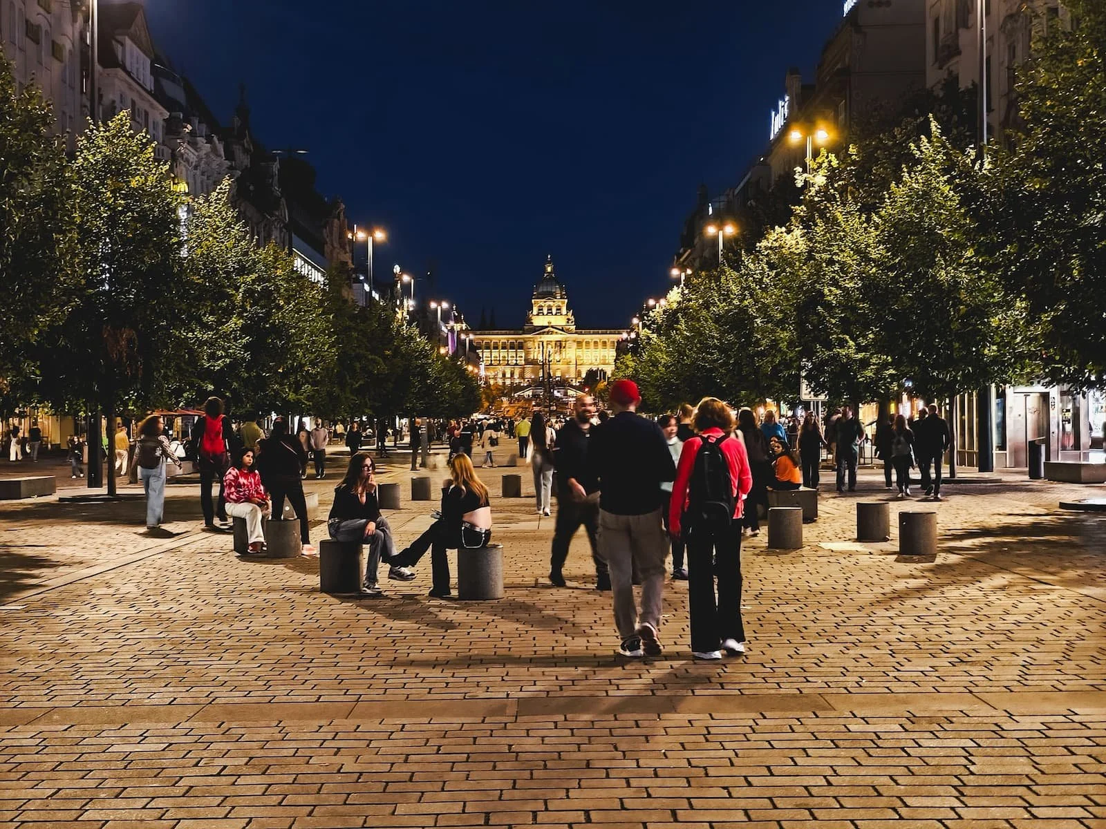 People walking along illuminated Wenceslas Square toward the National Museum at night.