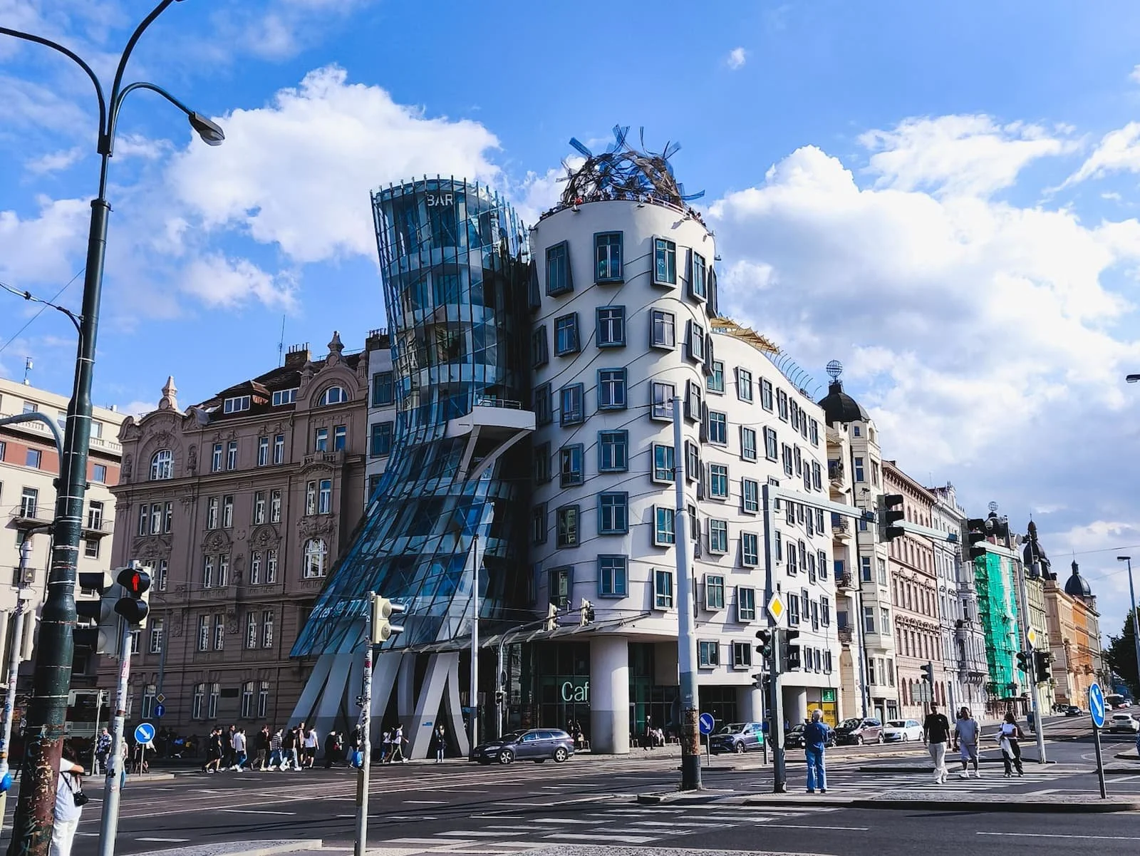 Curving glass and stone exterior of Prague's Dancing House against a blue sky.