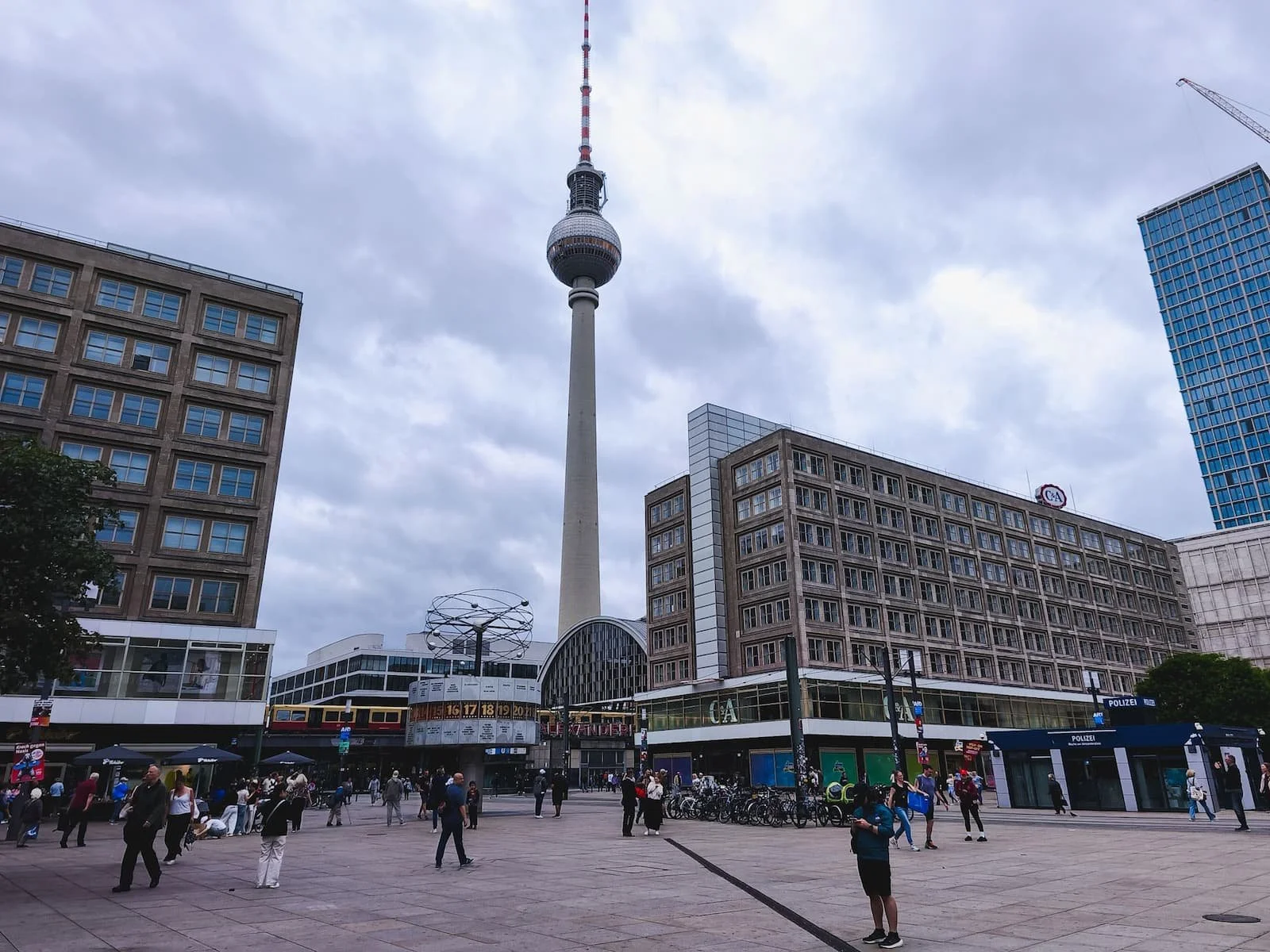 Berlin's Fernsehturm rising above Alexanderplatz, surrounded by modern buildings and pedestrians.
