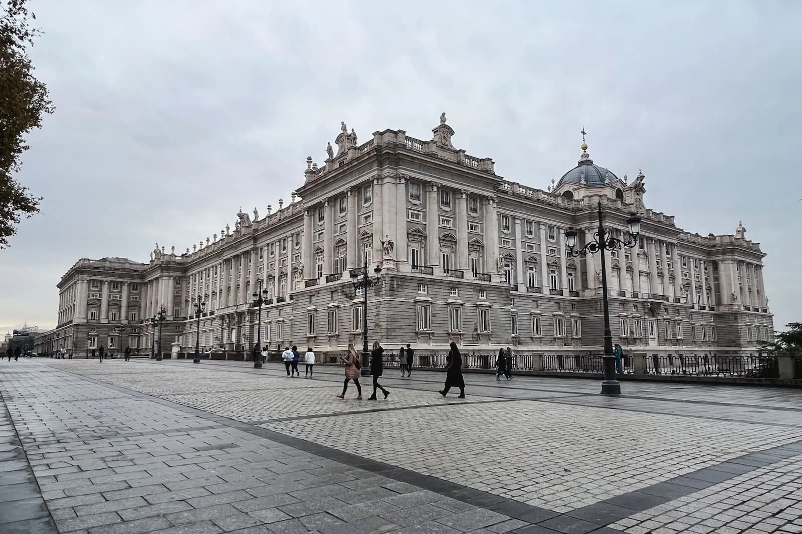 Royal Palace of Madrid exterior with open plaza and people walking.