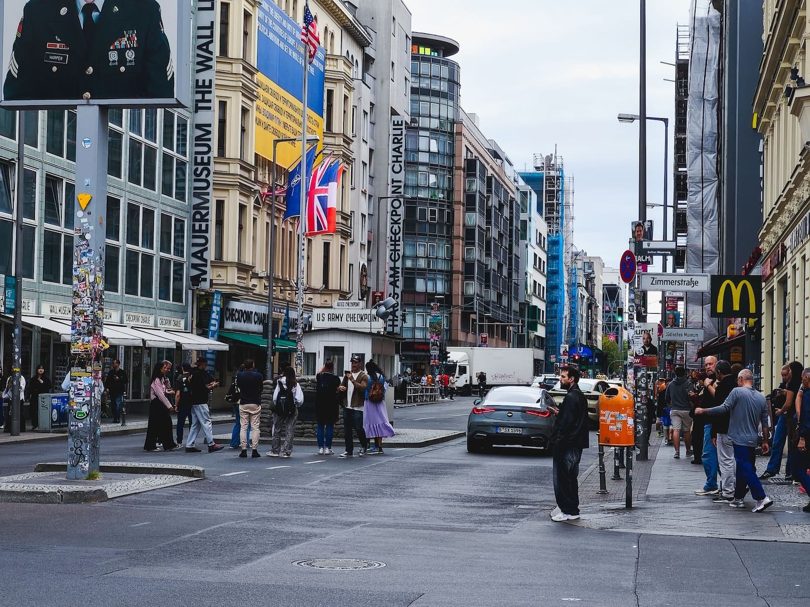 Checkpoint Charlie's reconstructed guardhouse in the middle of a busy Berlin street, surrounded by modern buildings.