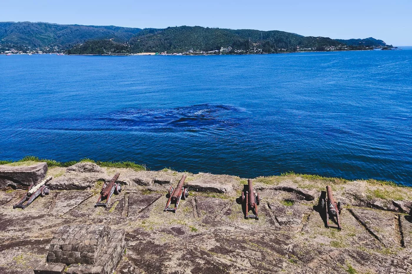 Historic cannons at Castillo de Niebla seen from above, with Valdivia’s bay in the background.