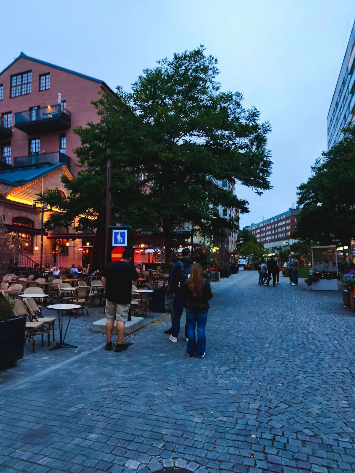 Pedestrian street near Signalfabriken in Sundbyberg, with outdoor restaurant seating, shops, and people walking.