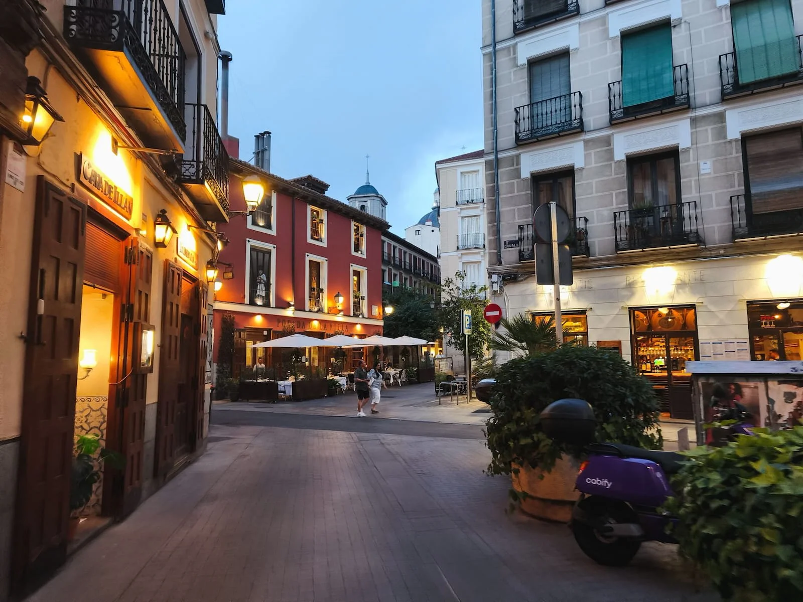Warmly lit taverns and outdoor tables on a street in La Latina at dusk