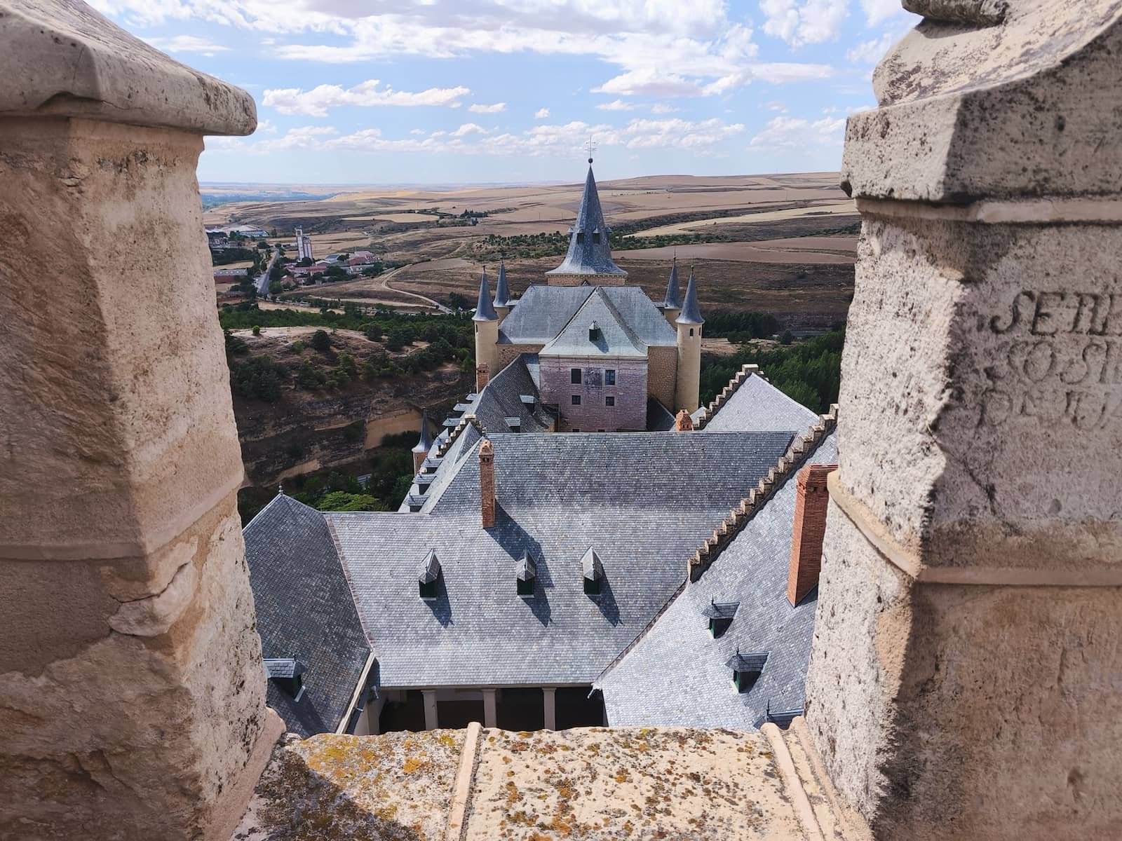View from the Alcázar of Segovia tower over the castle roof, valley, and surrounding landscape.