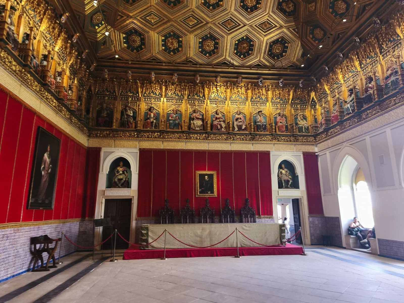 Hall of Kings inside the Alcázar of Segovia, with portraits, red walls, and a decorated ceiling.