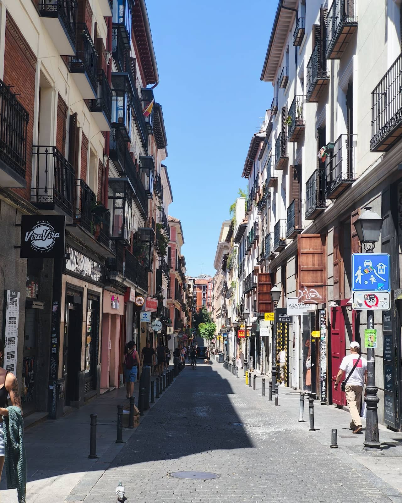 Narrow street in Madrid’s Malasaña neighborhood with balconies, shops, and pedestrians.