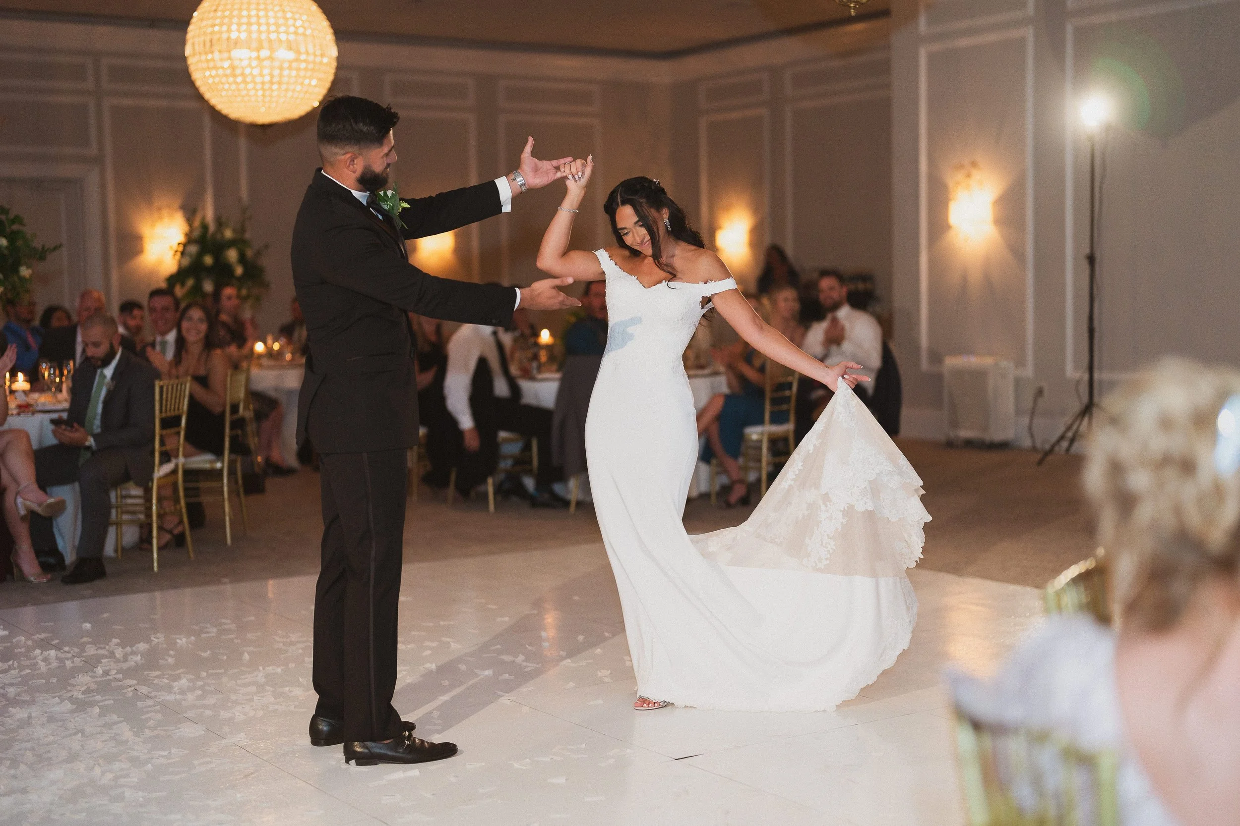 Bride and groom dancing at their wedding reception, with guests sitting at decorated tables watching.