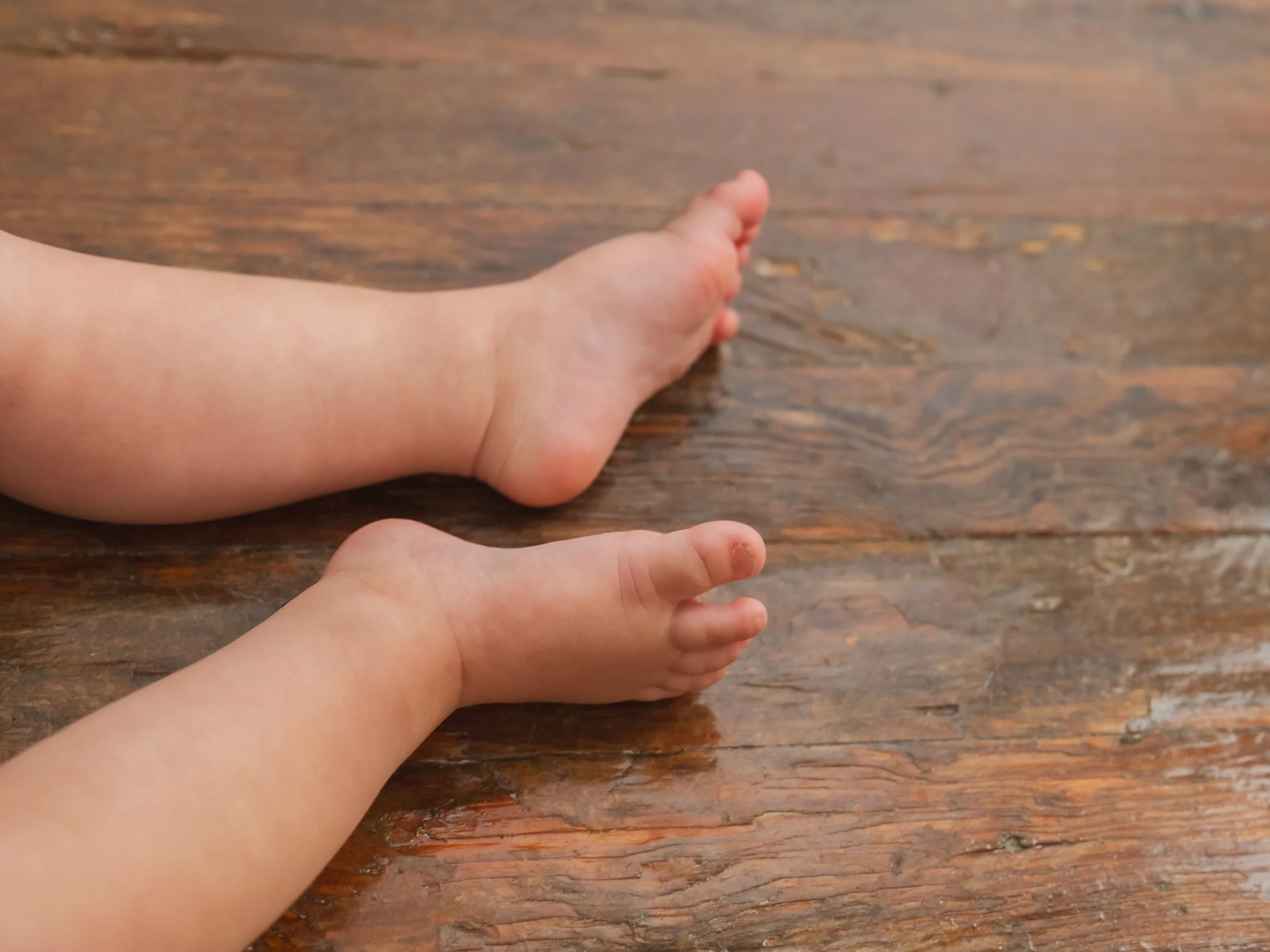 Close-up of a baby's chubby arm and hand resting on a wooden surface, with the hand's fingers curled slightly.