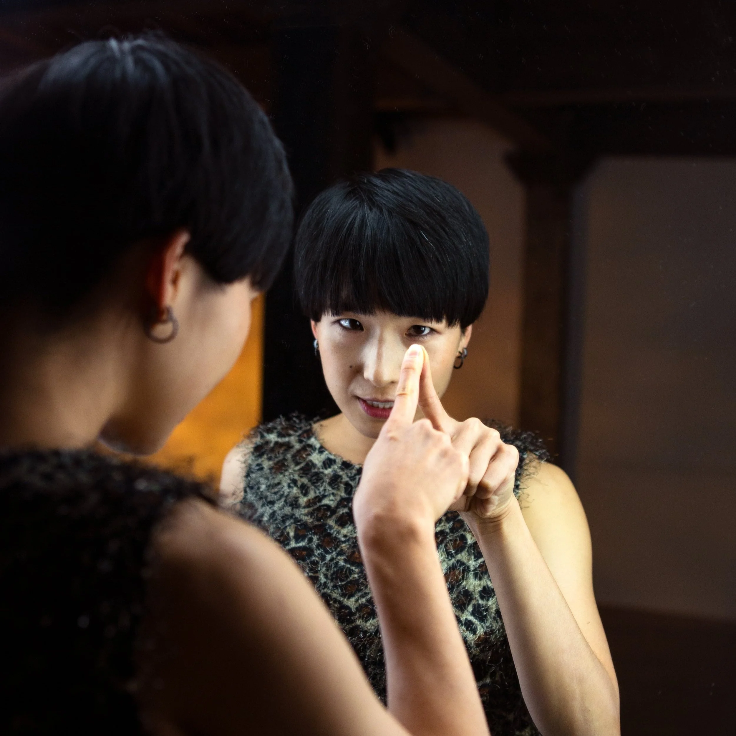 Hsiao-Jou in a cheetah print top in front of a mirror, pressing her finger against it
