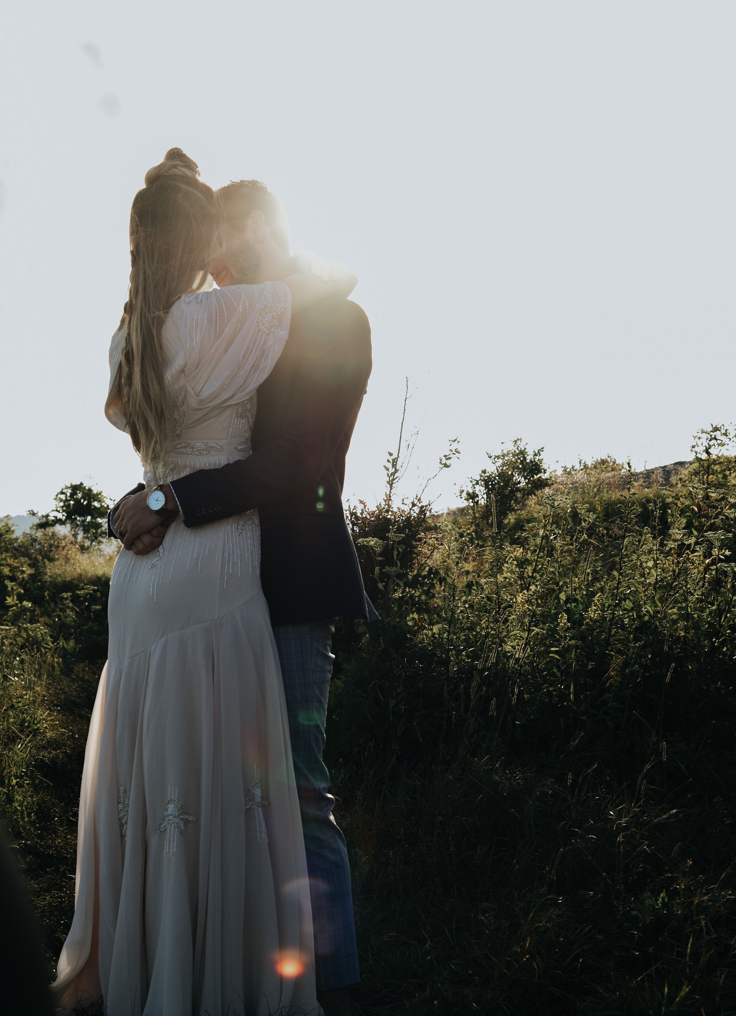  A photograph of a couple who have eloped, tenderly embracing outdoors in a field, as the sun shines behind them at a Black Balsam Knob elopement, southwest of Asheville, North Carolina 