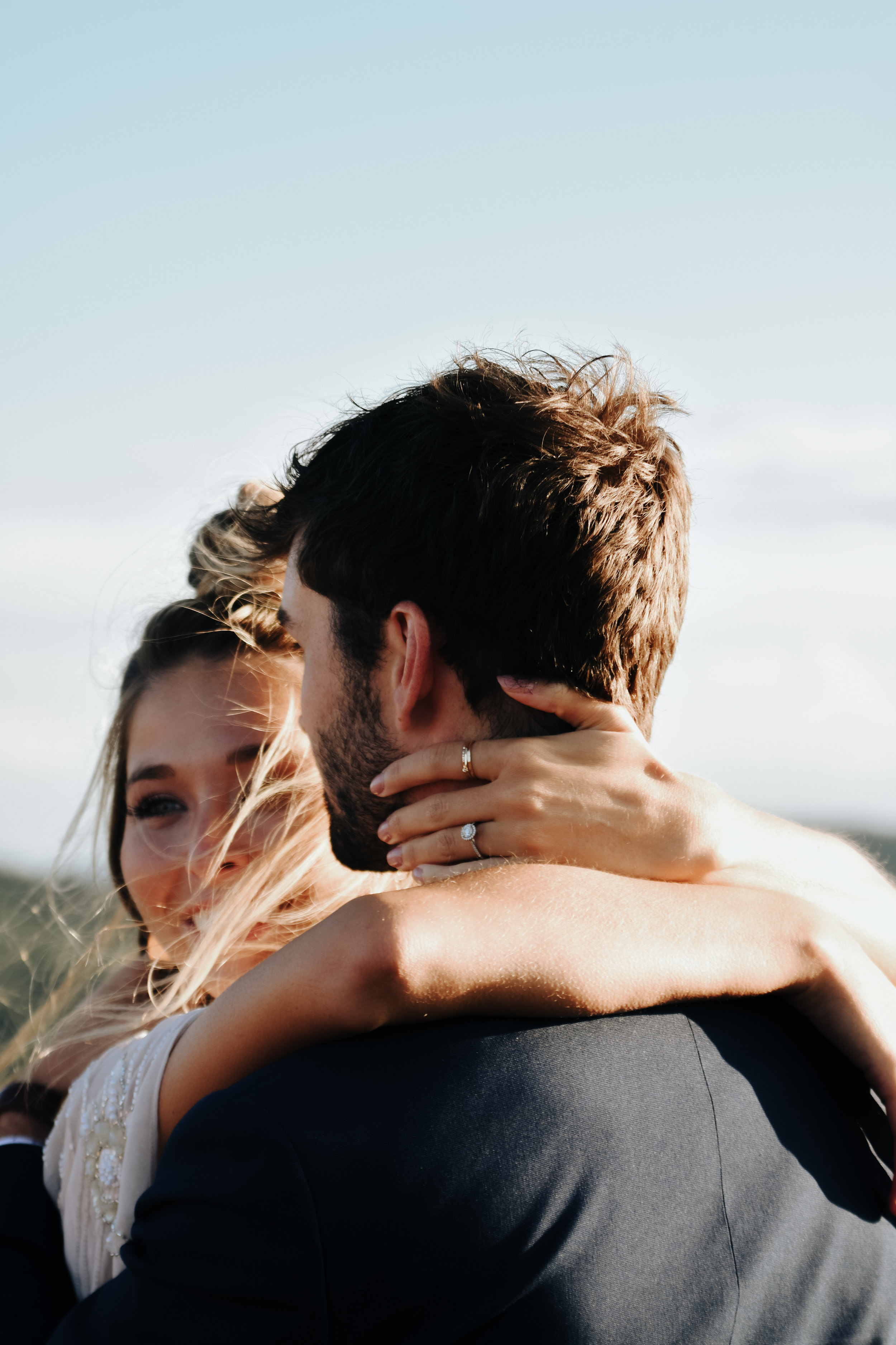  A picture of a closeup view of an eloped couple, with the bride wrapping her arms around her partner’s neck as the breeze blows her hair in the sunlight at Black Balsam Knob in the Blue Ridge Mountains 