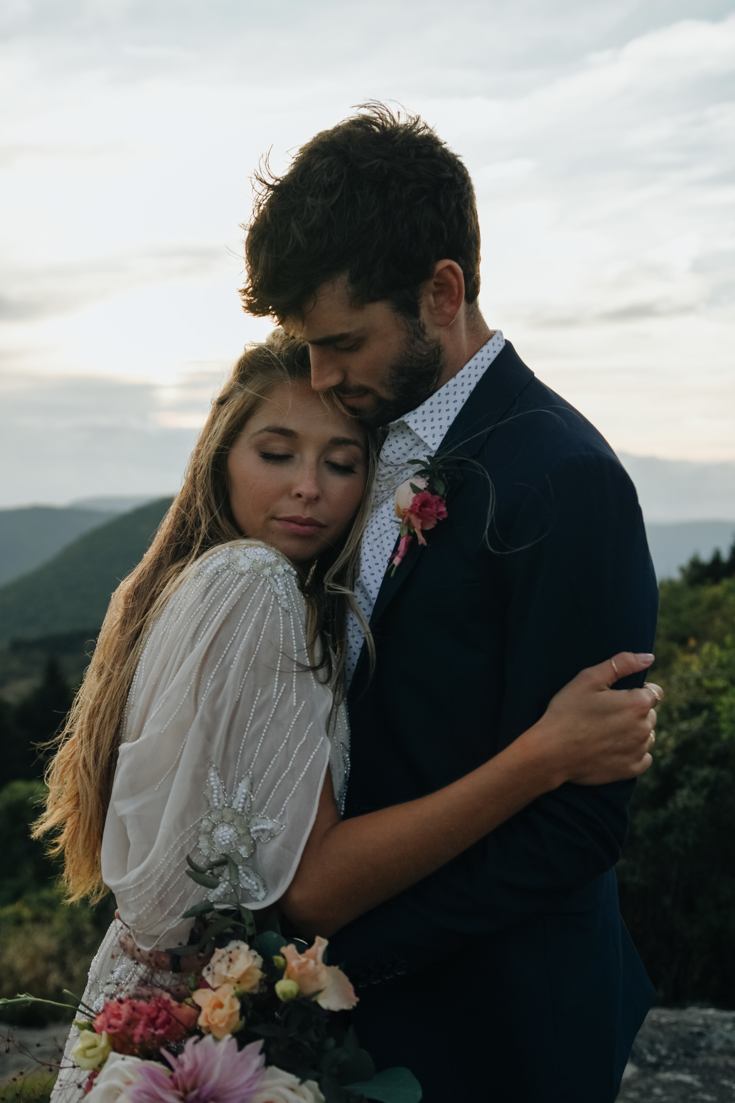  A picture of a couple after their elopement, romantically embracing each other closely as the bride rests her face against her partner’s chest while he tenderly leans his face down toward her at Black Balsam Knob, southwest of Asheville, North Carol