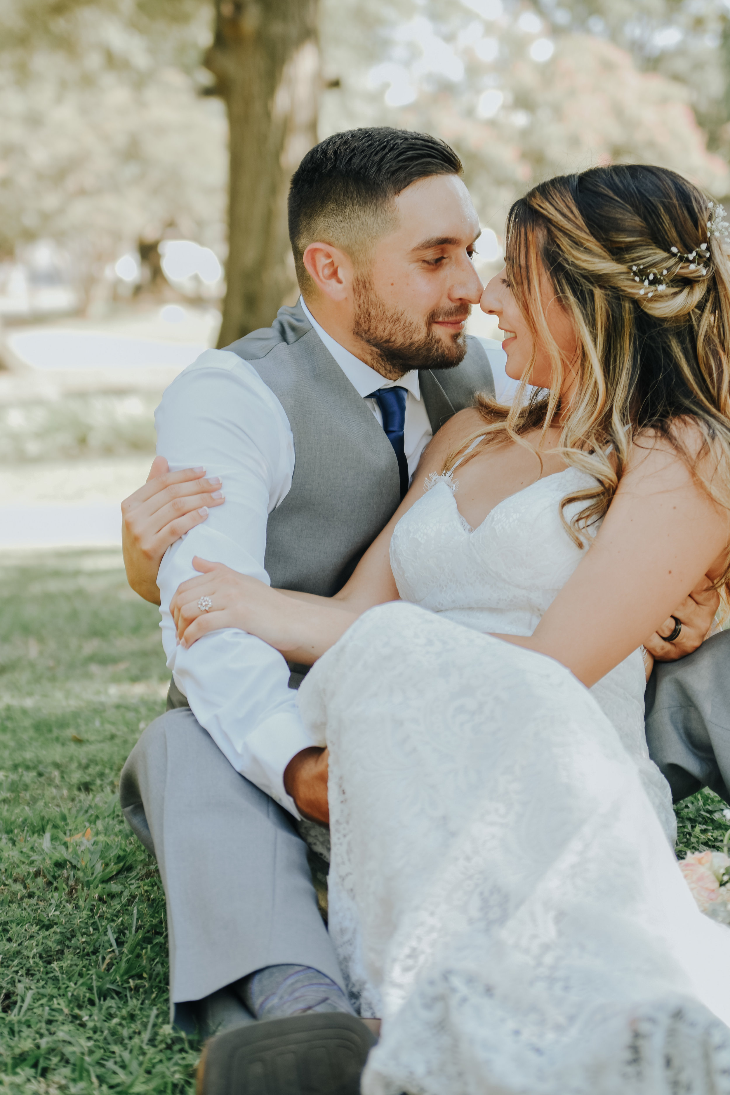  An image of a couple who just eloped, sitting in the grass, romantically embracing, touching noses and affectionately looking into each other’s eyes in Marshall Park by Vanessa Venable - Charlotte elopement photographer 