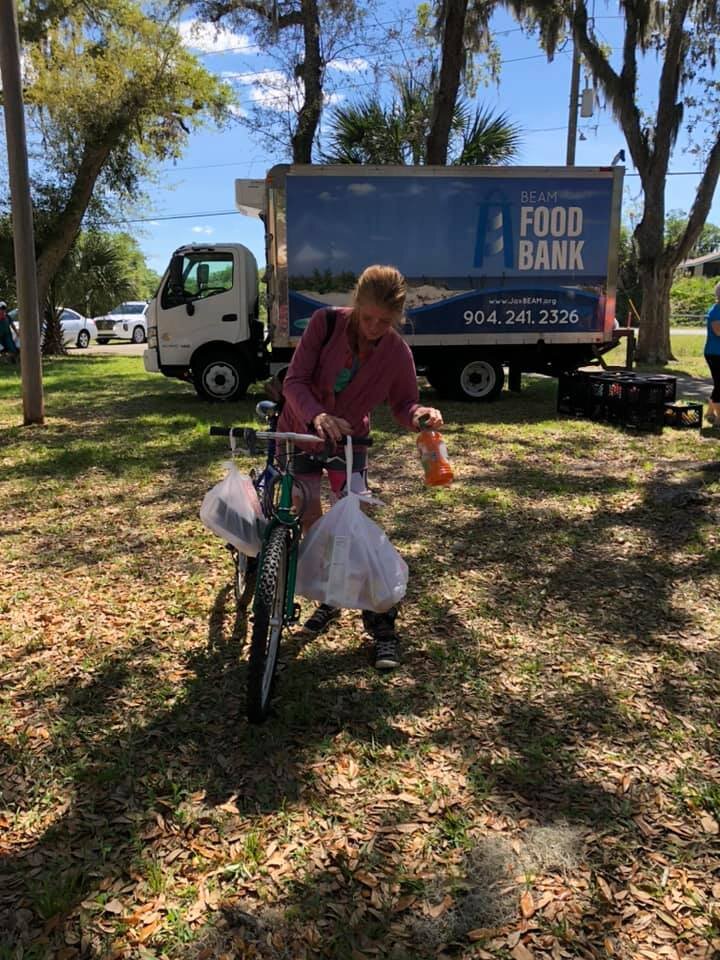 BEAM client balances her pre-packaged groceries on her bike received during the Mayport Mobile Pantry, before riding home