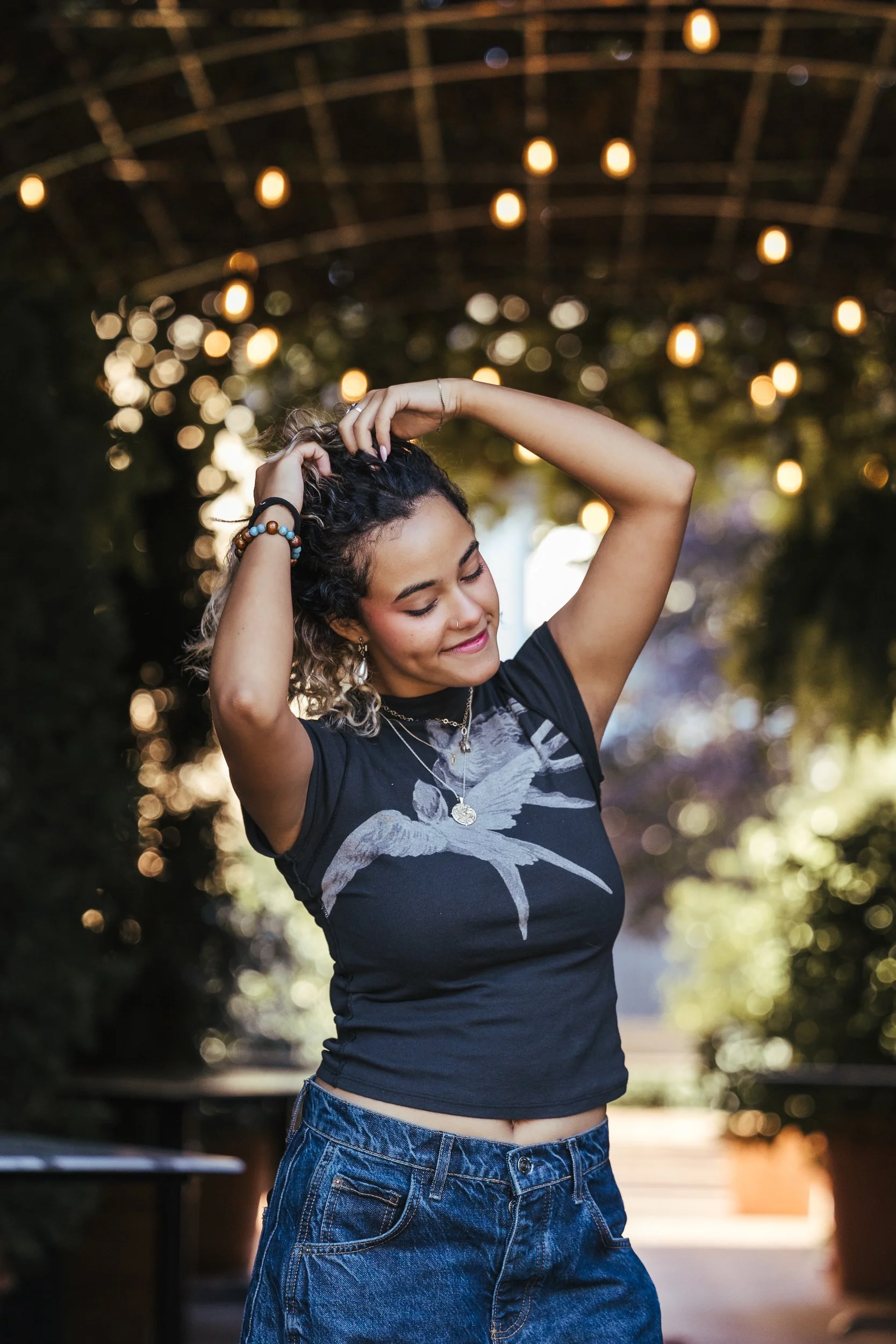 teen girl dancing with arms above head and blurred out twinkle lights in background