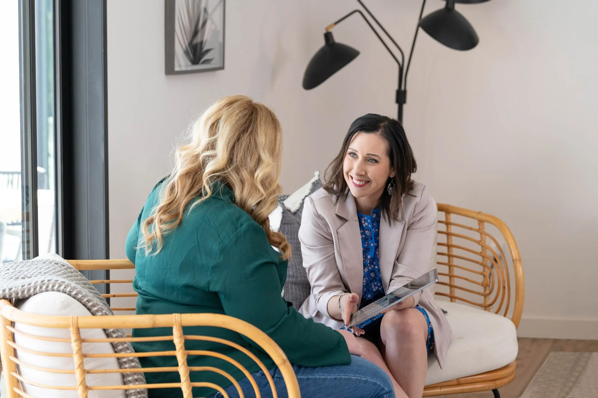 Two professional women sitting near a window reviewing content on a tablet