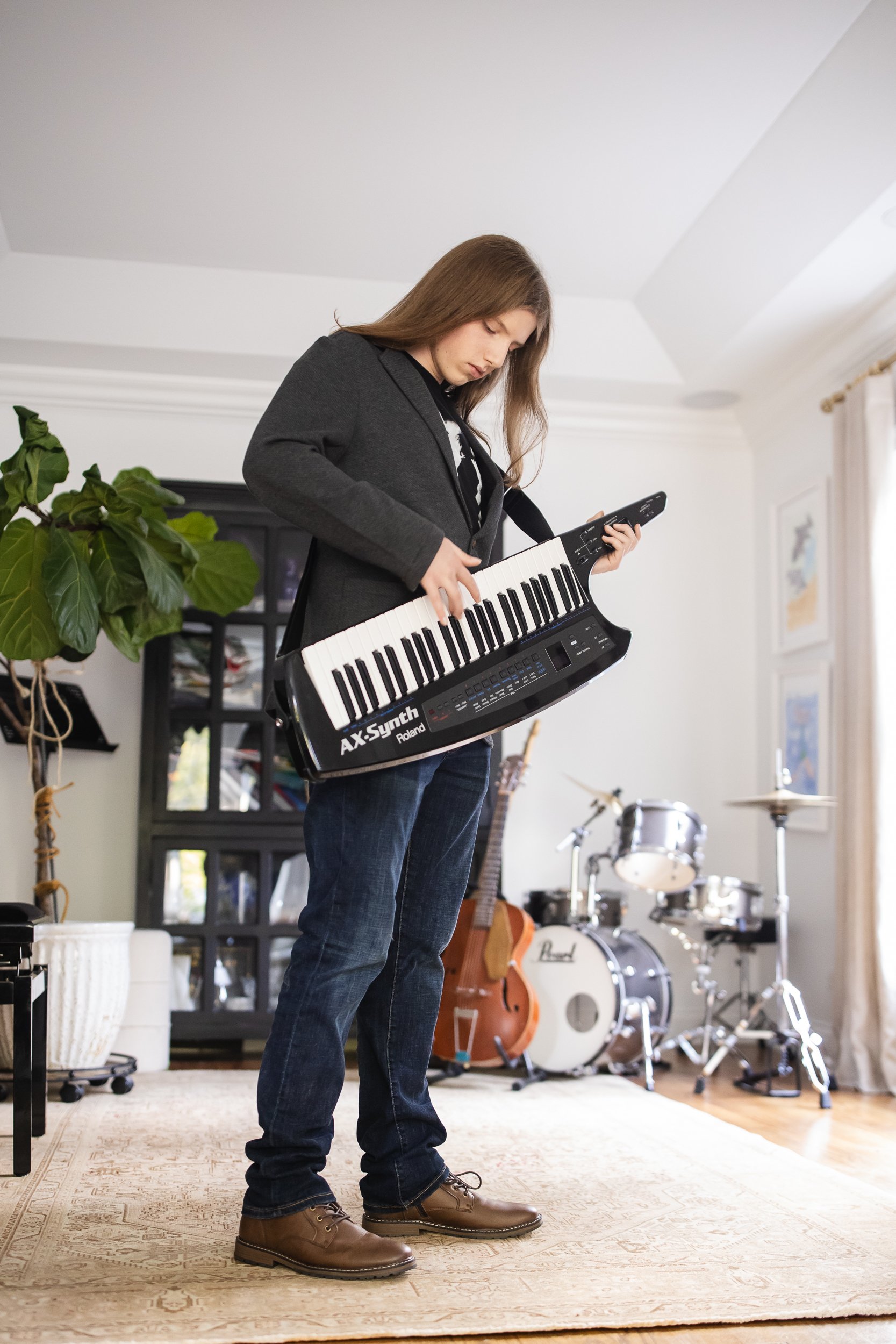 teen boy in his home playing a guitar with a drum set in the background
