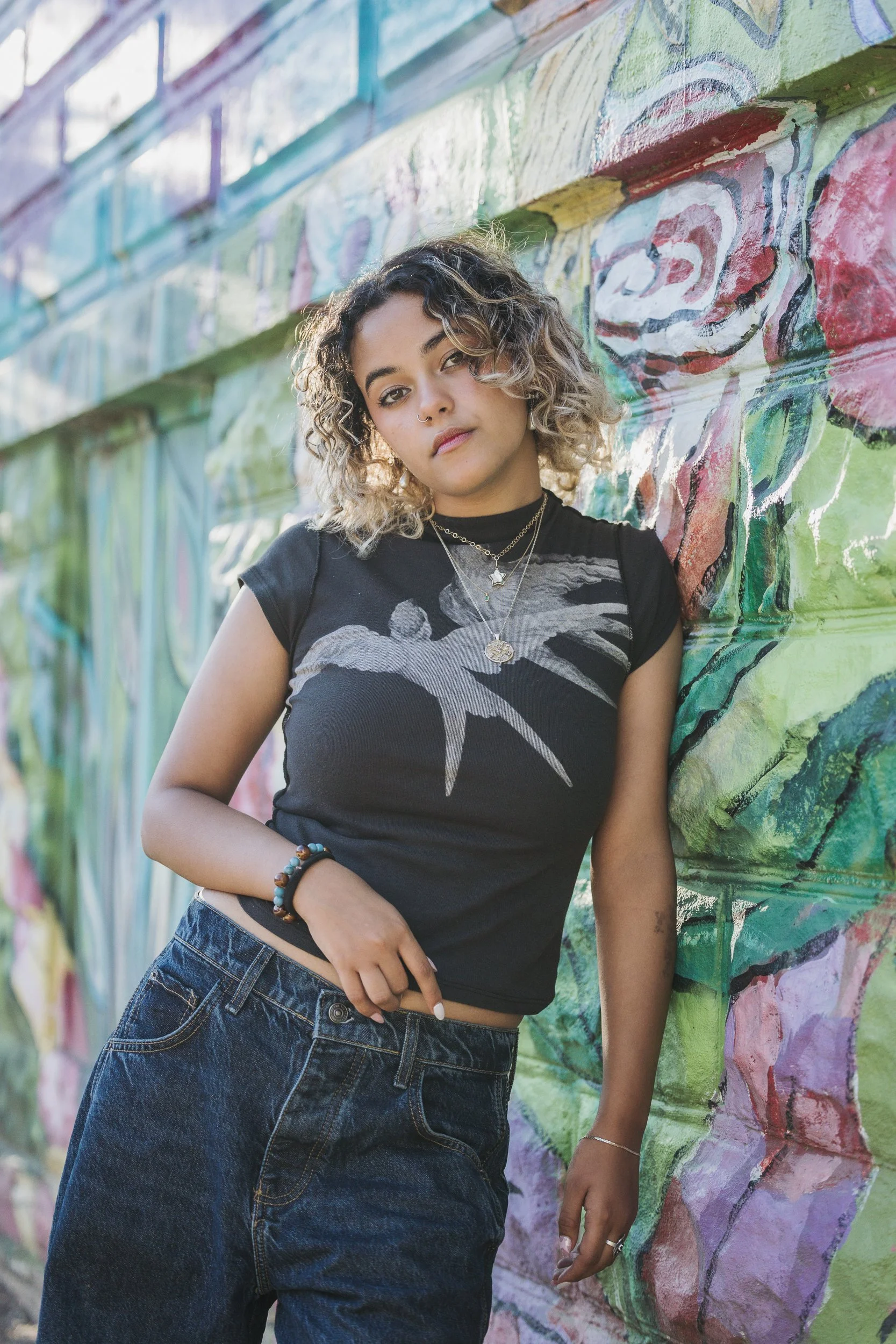 teen girl, leaning agains brick wall with colorful mural