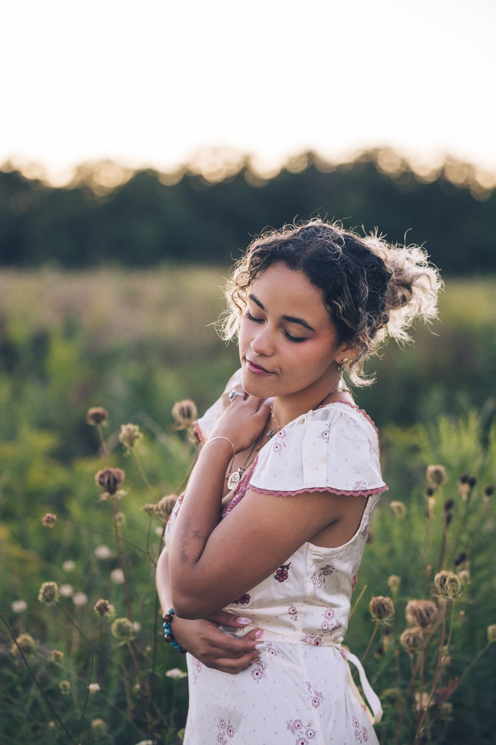 teen girl posed with her arms wrapped around her, standing in prairie grass at golden hour