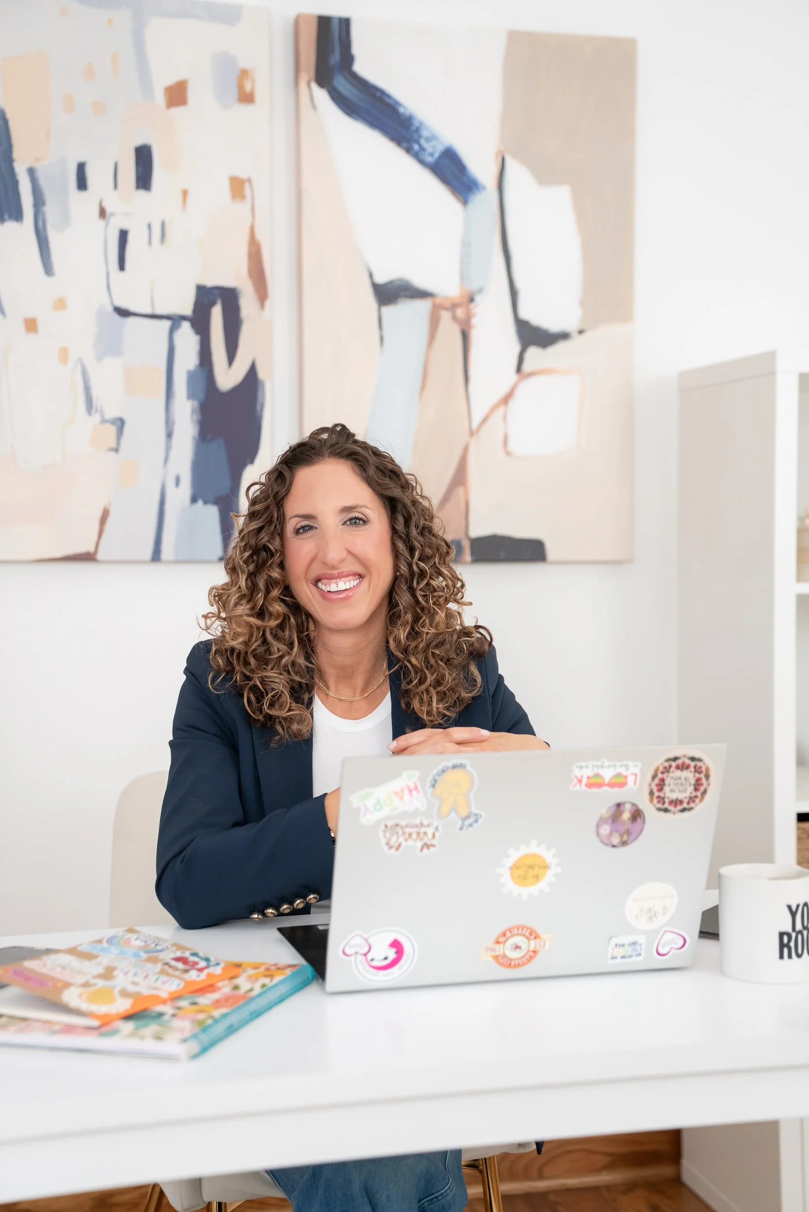 lifestyle headshot of a woman seated behind a desk in front of computer smiling at the camera