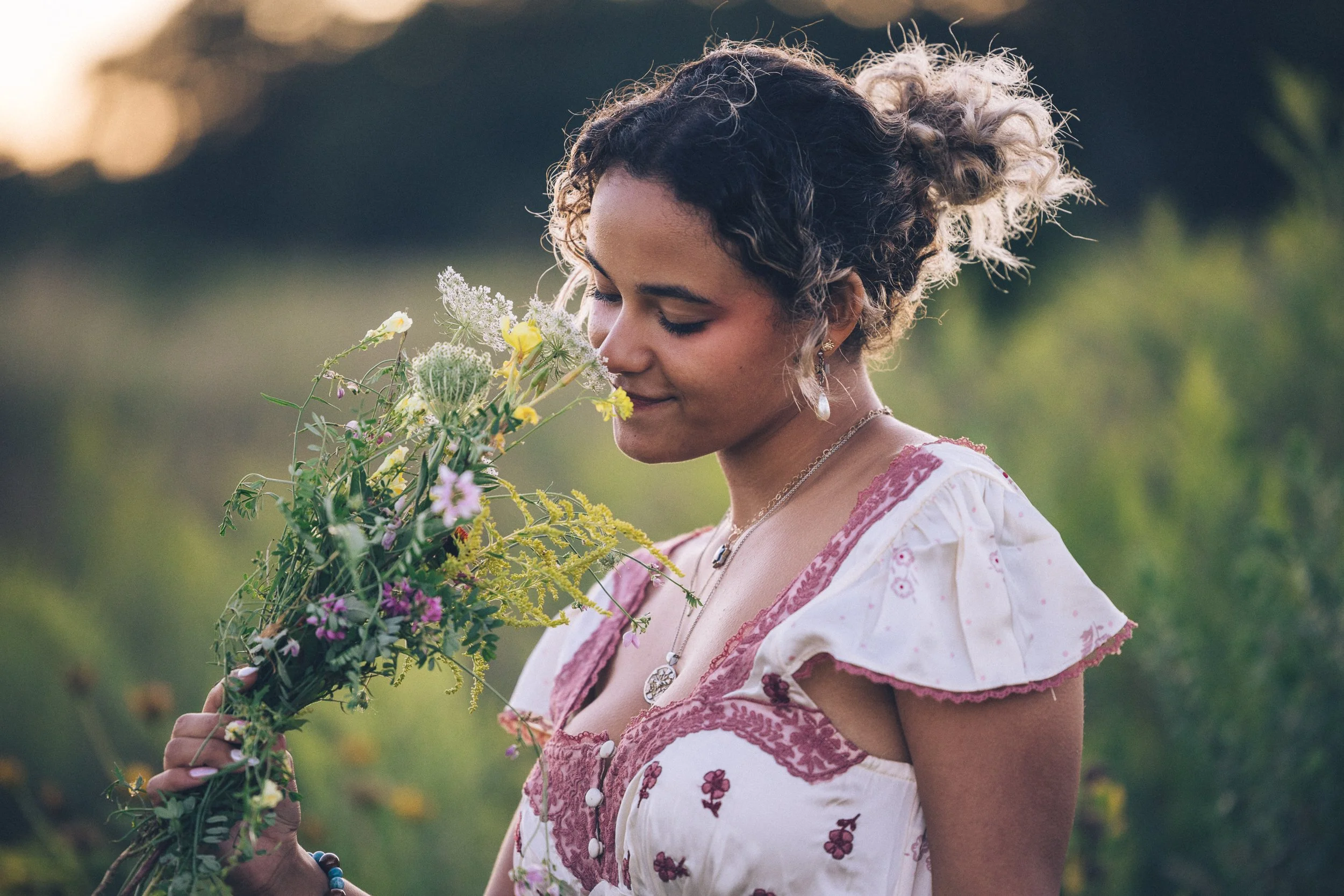 picture of a teen girl in a prairie at golden hour smelling a bouquet of wild flowers with a gentle smile