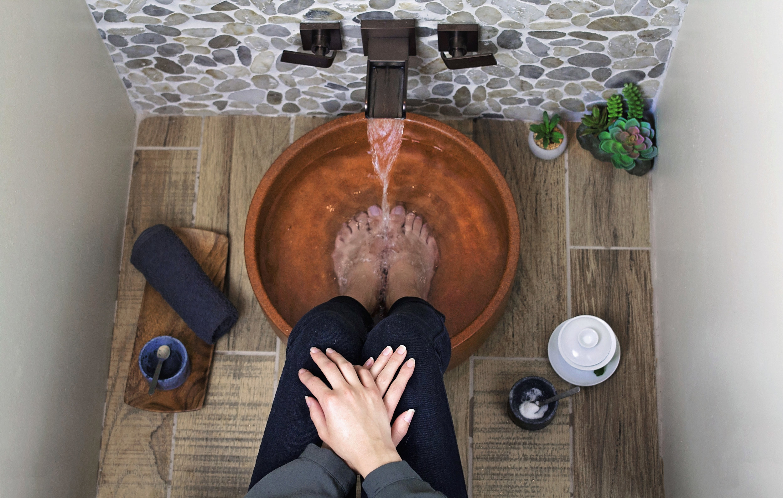 Woman crosses her hands over her lap while she waits for the water to fill in her aromatic foot bath at Jalan Facial Spa